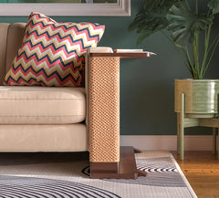 A Cat-e-Corner table placed next to a sofa, integrating a cat's scratching post with a small table, in a room with a plant and a colorful cushion.