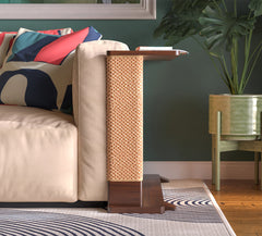 A Cat-e-Corner table placed next to a sofa, integrating a cat's scratching post with a small table, in a room with a plant and a colorful cushion.