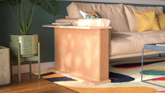 A Cat-e-Corner table placed next to a sofa, integrating a cat's scratching post with a small table, in a room with a plant and a colorful cushion.