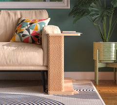 A Cat-e-Corner table placed next to a sofa, integrating a cat's scratching post with a small table, in a room with a plant and a colorful cushion.