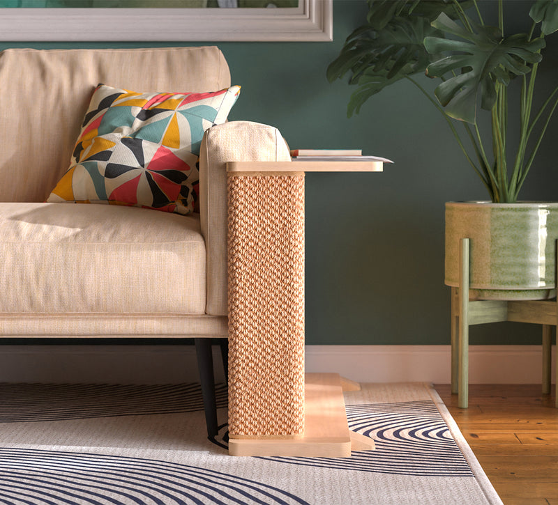 A Cat-e-Corner table placed next to a sofa, integrating a cat's scratching post with a small table, in a room with a plant and a colorful cushion.