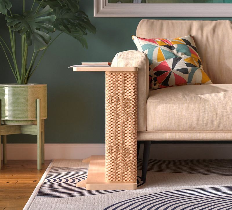 A Cat-e-Corner table placed next to a sofa, integrating a cat's scratching post with a small table, in a room with a plant and a colorful cushion.