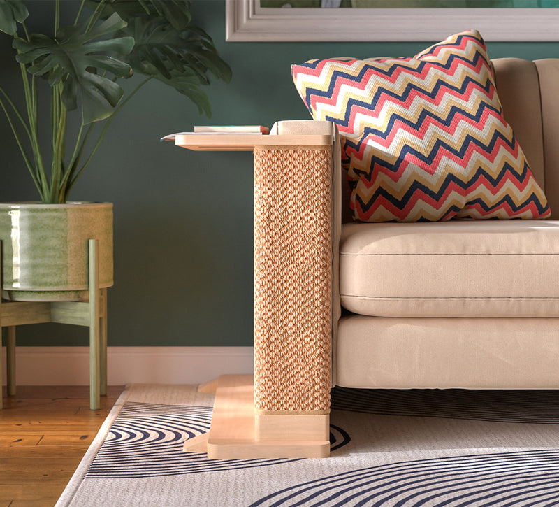A Cat-e-Corner table placed next to a sofa, integrating a cat's scratching post with a small table, in a room with a plant and a colorful cushion.
