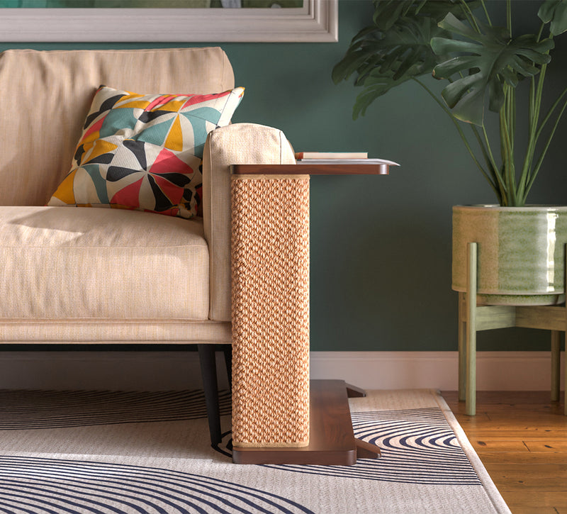 A Cat-e-Corner table placed next to a sofa, integrating a cat's scratching post with a small table, in a room with a plant and a colorful cushion.